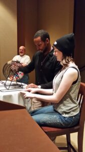 Two people playing bingo, one holding the cage with balls.