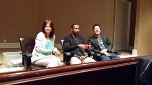Three people sitting on a bench indoors, smiling and posing for a photo.