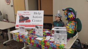 A child stands beside a colorful puzzle booth promoting autism awareness.