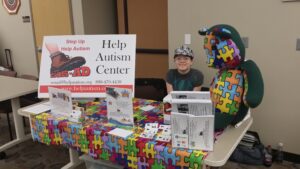 Child happily sitting in a colorful puzzle car at an autism center event.
