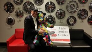 Man holding colorful teddy bear at Help Autism Center event.