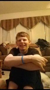 Smiling young person sitting on a couch with arms crossed.