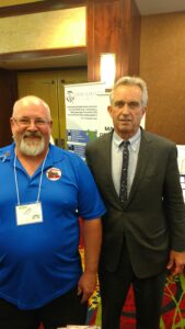 Two men posing for a photo at an event, one in a blue shirt, the other in a suit.