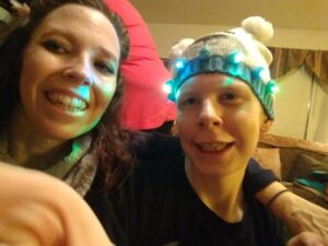 Two people smiling for a selfie indoors, one wearing a winter hat.