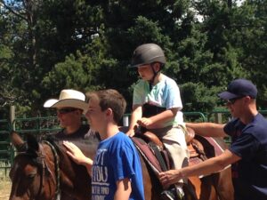A child wearing a helmet rides a horse with adults nearby.