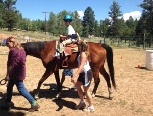 Child wearing helmet rides a horse with two adults assisting outdoors.