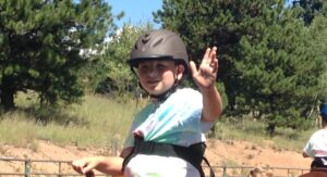 Child wearing a helmet outdoors making a peace sign.
