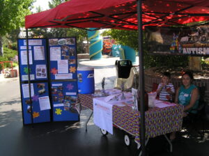 A small outdoor booth with informational boards and a seated person under a red canopy.
