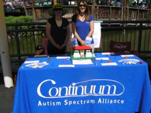 Two women at a Continuum Autism Spectrum Alliance information booth outdoors.