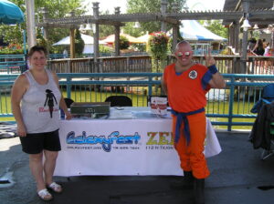 Two people at a booth, one dressed as Goku from Dragon Ball Z.