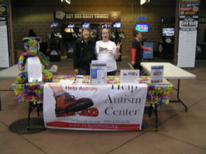 Two people stand behind an Amish Center information table at a public event.