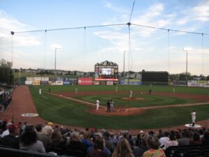 Crowd watches a baseball game at sunset in a packed stadium.