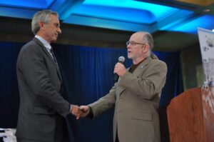 Two men shaking hands during a formal event with a microphone.