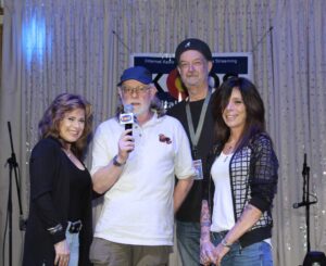 Four adults posing indoors, one holding a microphone.