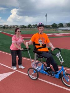 A man on a special bike holding hands with a woman on a running track.